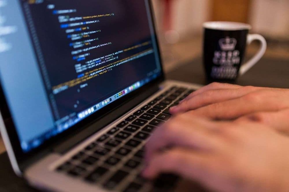 fingers typing code in laptop with black mug in the blurred background