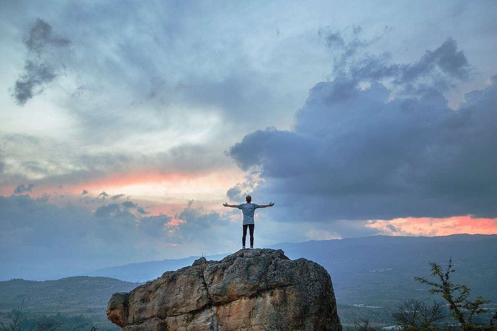 man standing on rock with stretched arms and looking at the sky
